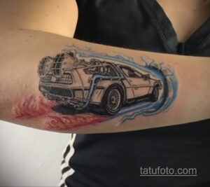 Фото татуировки DeLorean DMC-12 из фильма 'Назад в будущее' на руке. Изображение выполнено с эффектом движения и огня, с использованием синих и красных оттенков.