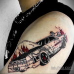 Фото тату на плече с изображением горящего DeLorean из фильма 'Назад в будущее' с языками пламени.