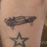 Черно-белое фото тату на руке, изображающее контурный рисунок автомобиля DeLorean из фильма 'Назад в будущее' и звезду.