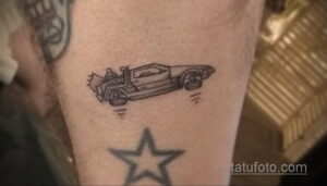 Черно-белое фото тату на руке, изображающее контурный рисунок автомобиля DeLorean из фильма 'Назад в будущее' и звезду.