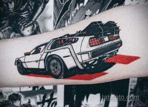Фото тату на предплечье с изображением задней части DeLorean из фильма 'Назад в будущее' в черно-красной гамме, с эффектом скорости.