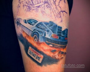 Фото тату на руке с изображением DeLorean, летящего в воздухе. Динамичный рисунок с эффектом скорости и огня.