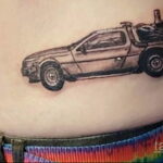 Фото тату: Черно-белый рисунок DeLorean на женском боку. Детализированная проработка автомобиля, реалистичное изображение, минималистичный стиль.