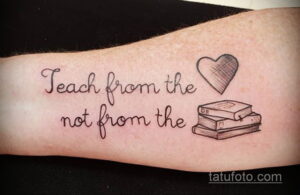 Фотография черно-белой татуировки на руке, изображающей цитату 'Teach from the heart not from the book' и стопку книг с сердцем. Татуировка выполнена в минималистичном стиле.