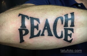 Фото черно-белой татуировки с надписью 'Teach Peace' выполненной стилизованным шрифтом на руке.