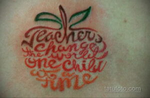 Фото тату надписи 'Teachers change one child at a time' в форме красного яблока с зелеными листьями на руке.