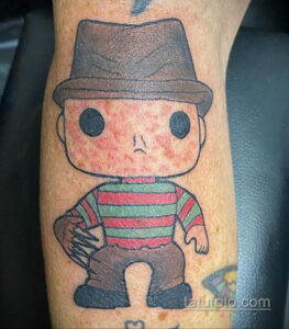 Фото тату Фредди Крюгера на руке в стиле Funko Pop. Изображение выполнено в мультяшном стиле с большими глазами и упрощенными формами.