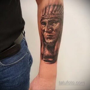 Фото тату: реалистичный портрет индейского вождя в профиль, выполненный в черно-серых тонах на предплечье руки.