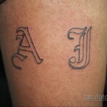 Фото тату с инициалами 'A' и 'J', выполненное в черно-серых тонах на запястье. Изящный шрифт с тонкими линиями.