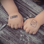 Фото тату на руках пары: надпись 'LUCKY' на одной руке и контур сердца со стрелой на другой. Минималистичный дизайн, символизирующий удачу и любовь.