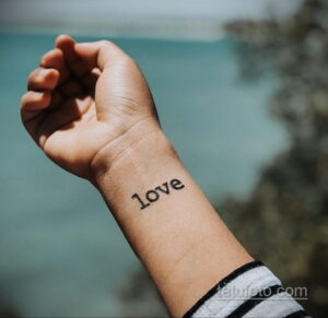 Фото тату надписи 'love' на запястье, выполненное простым шрифтом. Небольшой и лаконичный рисунок татуировки.