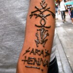 Фото тату мехенди: рука, украшенная сложным узором хной, с надписью "Sara's Henna" и символическими элементами.