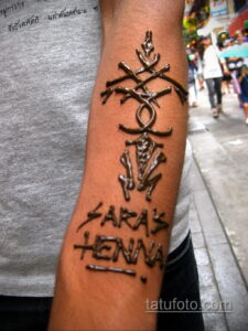 Фото тату мехенди: рука, украшенная сложным узором хной, с надписью "Sara's Henna" и символическими элементами.