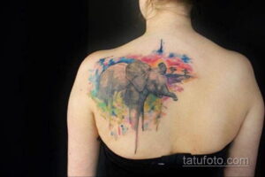 Фото тату: Изображение слона, выполненное в технике акварельной татуировки с использованием ярких и насыщенных цветов на спине. Красивый и оригинальный рисунок татуировки.