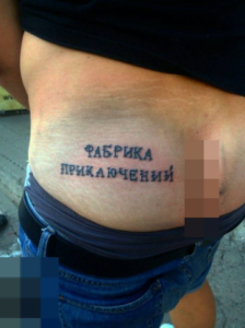 Фото татуировки надпись на боку женщины. Черная надпись 'ФАБРИКА ПРИКАЧЕНИЙ' выполнена простым шрифтом. Минималистичный рисунок татуировки.