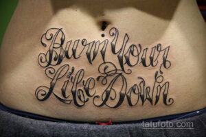 Фото тату на животе: надпись "Burn Your Life Down" в готическом стиле. Черная татуировка, выражающая бунтарский дух.
