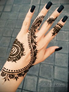 Фото тату мехенди на руке с черными ногтями. Детализированный узор с геометрическими элементами и тонкими линиями, выполненный в традиционном стиле.