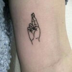 Фото тату с минималистичным рисунком двух рук, сложенных в жест 'finger guns', на запястье. Черные линии, тонкая работа.