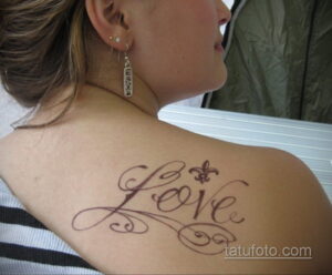 Фото тату надписи 'Love' с изображением лилии на спине девушки. Элегантный и романтичный рисунок татуировки, выполненный в мягких тонах.