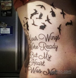 Фото тату на спине: стая летящих птиц и надпись 'Your Wings Were Ready But My Heart Was'. Черно-серые тона, каллиграфический шрифт, эмоциональный и трогательный дизайн.