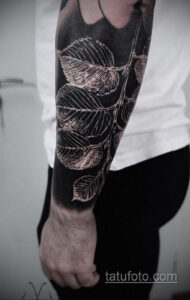 Фото тату с изображением ветки с листьями, выполненной в технике blackwork на руке мужчины. Детализированный рисунок с использованием только черного цвета.