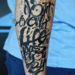 Фото татуировки надписи "Don't waste life" на руке мужчины. Рисунок выполнен в стиле граффити черными чернилами.