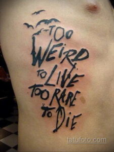 Фото тату на груди: надпись "Too Weird to Live Too Rare to Die" и силуэты летучих мышей. Рисунок татуировки в стиле леттеринг.
