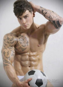 Фото тату: мужчина с татуировками в стиле племенного орнамента на плечах и руках, держащий футбольный мяч.