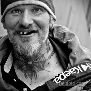 Фото татуировки на шее и груди мужчины в черно-белом стиле. Изображен череп с розами и надписями.
