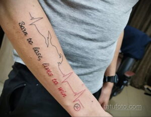 Фото минималистичной татуировки на предплечье, изображающей кардиограмму и надпись 'Born to lose, lives to win'.