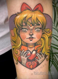 Фото тату на предплечье с изображением Sailor Moon, держащей в руках сердце. Рисунок выполнен в стиле аниме с яркими цветами и четкими линиями.