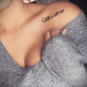 Фото тату с надписью 'Faith is with me' на плече девушки. Минималистичный шрифт, черные чернила, нежная кожа.