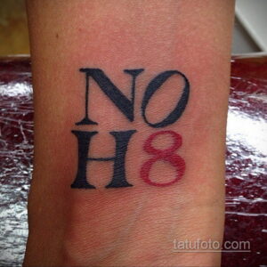 Фото тату на запястье с надписью 'No H8' в стильном шрифте, выполненное в черно-красной гамме. Символ поддержки равенства.