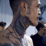 Фото тату: красочная татуировка совы на шее мужчины. Использованы яркие цвета и традиционный стиль.