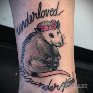Фото тату опоссума на предплечье с надписью 'underloved' и 'misunderstood', выполненное в реалистичном стиле с использованием черных и серых оттенков.