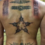 Фото тату: сложный узор тайской сакральной геометрии и символов на всей спине мужчины. Черно-белая татуировка в традиционном стиле.