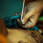 Фото тату: крупный план руки мастера тату, наносящего рисунок на кожу. Видны детали тату-машинки и процесса нанесения.