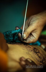 Фото тату: крупный план руки мастера тату, наносящего рисунок на кожу. Видны детали тату-машинки и процесса нанесения.