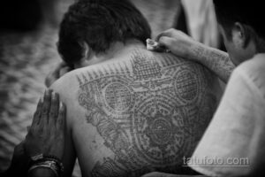 Фото тату: Мастер наносит сложную тайскую татуировку на спину мужчины. Черно-белое фото, демонстрирующее процесс нанесения.