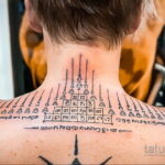 Фото тату: сакральная татуировка с иероглифами и символами, расположенная на шее и верхней части спины мужчины. Детализированный рисунок татуировки в стиле сак янт.