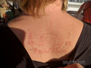 Фото тату: крупный план свежей татуировки на спине, показывающий покраснение и небольшие ранки в процессе заживления.