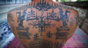 Фотография мужской спины, покрытой сложными татуировками в тайском стиле, состоящими из черных линий и символов.