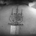 Фото тату: небольшая татуировка на затылке, изображающая сакральный символ, выполненная черными линиями. Детальный рисунок татуировки.