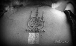 Фото тату: небольшая татуировка на затылке, изображающая сакральный символ, выполненная черными линиями. Детальный рисунок татуировки.