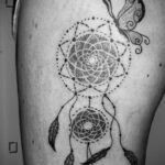 Фото тату ловца снов, выполненного в технике dotwork. Рядом с ловцом снов изображена бабочка. Черно-белая татуировка на руке.