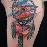 Фото тату: Красочная акварельная татуировка с ловцом снов на плече. Использование ярких цветов и плавных переходов.