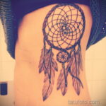 Фото тату ловца снов в стиле blackwork на боку. Детализированный рисунок с подвесками из бисера и перьями. Идеально для поклонниц этнических мотивов.