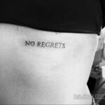 Фото тату: простая черная надпись 'No Regrets' на боку женщины, выполненная тонким шрифтом. Минималистичный стиль.