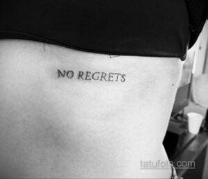 Фото тату: простая черная надпись 'No Regrets' на боку женщины, выполненная тонким шрифтом. Минималистичный стиль.