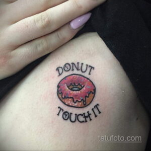 Фото тату пончика с короной и надписью 'DONUT TOUCH IT' на запястье. Черно-белый рисунок, выполненный в минималистичном стиле, с юмористическим подтекстом.